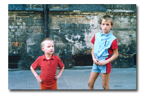 Zwei Jungen, ca. 4 bzw 7 Jahre alt, vor einer Mauer stehend